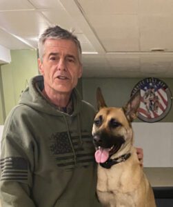 Man in hoodie posing with a happy German Shepherd indoors.